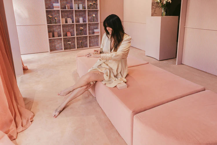 Woman sitting on a pink bench in a stylish room with shelves and decor.